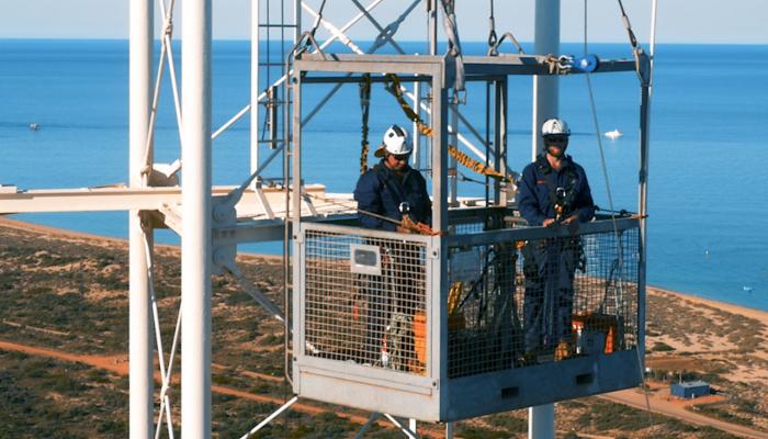 Two workers standing in communication tower. Ocean in background.